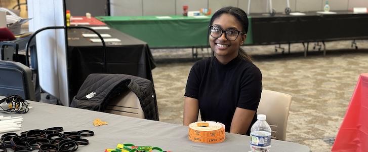 Student seated at event table and smiling
